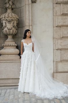 a woman in a white wedding dress standing next to a stone wall and wearing a long veil