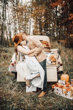 a man and woman kissing in front of an old truck with pumpkins on the ground