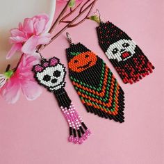 three beaded earrings are sitting on a pink surface next to a branch with flowers