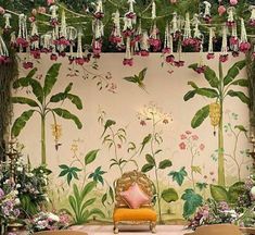 a room decorated with flowers and greenery on the wall, chairs are in front of it