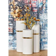 three white vases with flowers in them on a wooden floor next to a painting