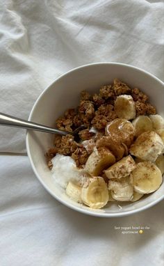 a bowl filled with granola and bananas on top of a white cloth covered table