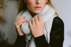 a woman wearing a white scarf and two gold rings on her finger, standing in front of a wall