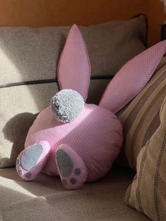 a pink bunny stuffed animal sitting on top of a couch next to pillows and throw pillows