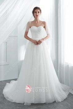 a woman in a white wedding dress standing by a window with her hands on her hips