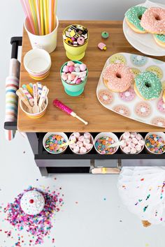 a wooden table topped with lots of donuts and sprinkles on top of it