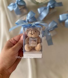 a small teddy bear in a clear box with blue ribbon around the neck and name on it