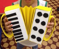 a young boy holding up an accordion made out of paper with black and white piano keys