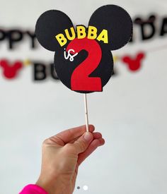 a person holding up a mickey mouse cake topper with the number 2 on it