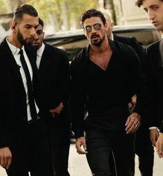 three men in suits and ties walking down the street with one man wearing sunglasses on his head