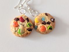 two cookies with candy and candies on them are hanging from silver earwires