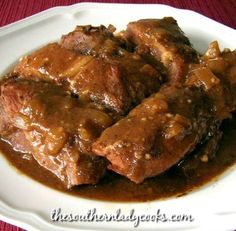 the meat is covered in gravy on the white plate with red table cloth