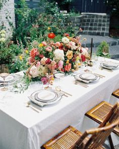 a table set with plates and flowers on it for an outdoor dinner party in the garden