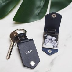 two leather keychains with the word dad printed on them next to a plant