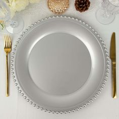 a white plate with silver beaded trim and gold forks, knives and spoons