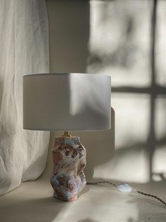 a table lamp sitting on top of a white surface next to a window with sheer curtains