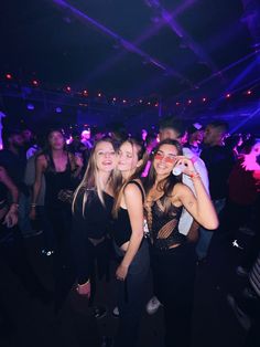 three young women standing next to each other in front of a crowd at a party