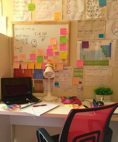 a desk with a laptop computer sitting on top of it next to a wall covered in sticky notes