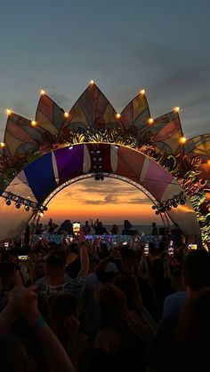 an outdoor concert with lots of people watching the sun go down and lights on their cell phones