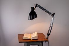 an open book sitting on top of a wooden table next to a black desk lamp