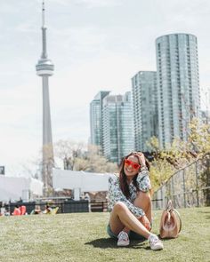 a woman sitting in the grass with her hand on her head and wearing red sunglasses