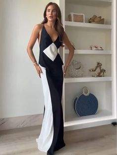 a woman in a black and white dress standing next to a book shelf with shoes on it