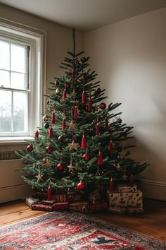 a small christmas tree with ornaments on it in front of a large window and rug