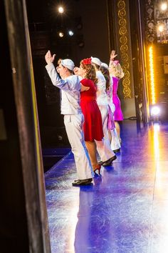 a man and woman dancing on stage with their arms in the air while other people watch