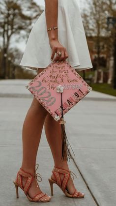 a woman in high heels holding a pink graduation cap and tasseled clutch bag