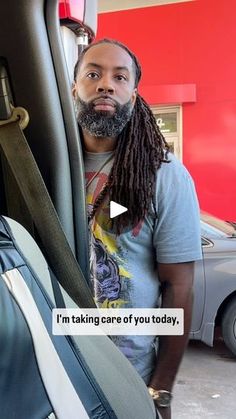 a man with dreadlocks standing next to his luggage in a car dealership