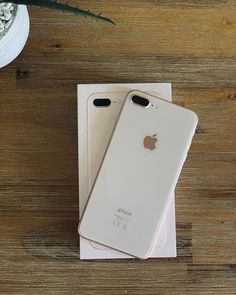 two white iphones sitting on top of a wooden table next to a flower vase