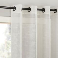 white curtains hanging on the side of a window with black metal rods and an open window pane