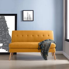 a yellow couch sitting in front of a window next to a black framed picture on the wall