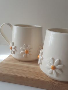 two white mugs sitting on top of a wooden board next to each other with flowers painted on them