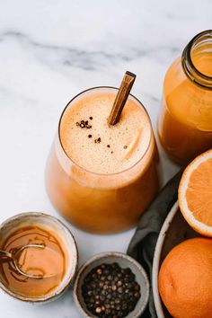 two glasses filled with orange juice next to some sliced oranges and cinnamon on a table