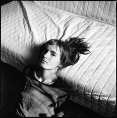 a black and white photo of a woman laying on a bed with her hair blowing in the wind