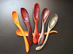 five spoons are lined up next to each other on a black counter top with yellow and orange handles