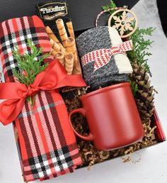 a red coffee mug sitting on top of a box filled with blankets and other items