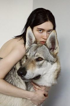 a woman is hugging a wolf with her arms wrapped around her chest and looking at the camera