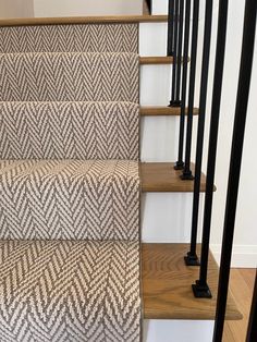 some stairs with carpet on them and black handrails in the middle, next to white walls