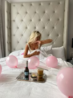 a woman laying in bed surrounded by pink balloons