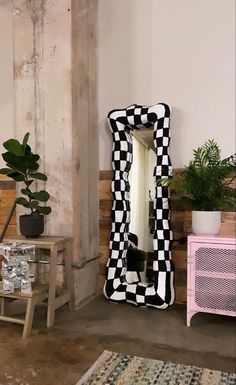 a black and white checkerboard mirror sitting on top of a wooden floor next to a pink table