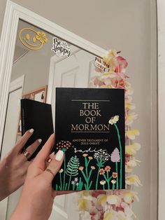 the book of mormon is being held up in front of a mirror with flowers on it