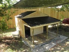 a dog house built into the side of a fenced in area with grass and trees