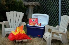 two lawn chairs sitting in the grass next to an ice chest and fire pit,