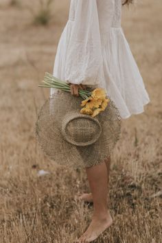 a woman in a white dress holding a straw hat and flowers