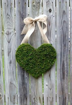 a heart shaped moss plant hanging on a wooden fence with a ribbon tied around it