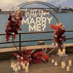 a sign that says will you marry me? surrounded by flowers and candles