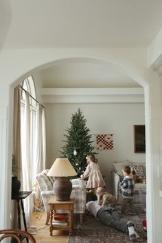 two people sitting on the floor in front of a christmas tree with a little boy standing next to them