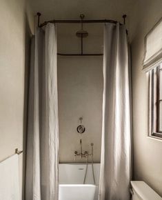 a white bath tub sitting under a window next to a toilet in a room with curtains